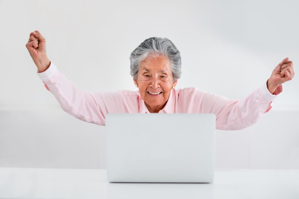 Elder woman celebrating her online success with arms up