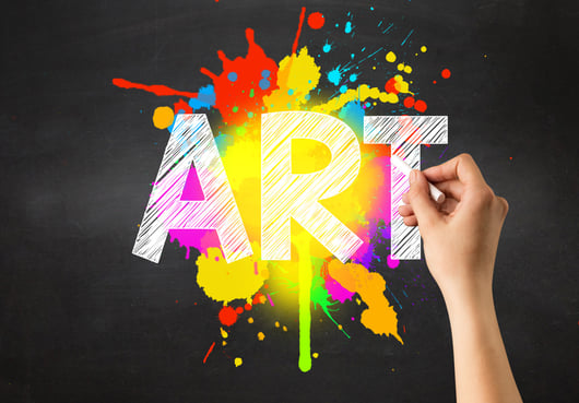 Female hand holding white chalk in front of a blackboard with art written on it and a colorful splash in the background