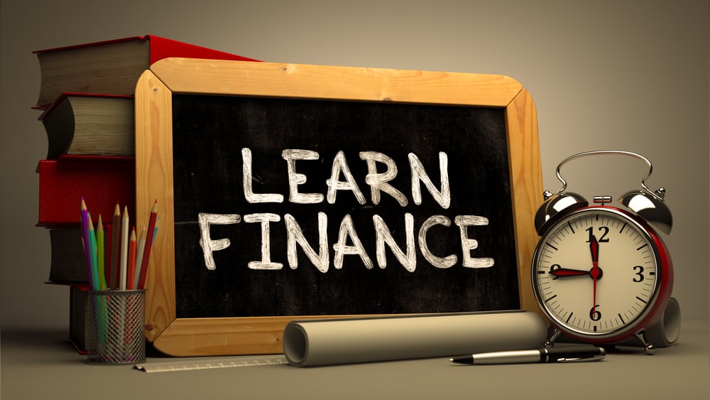 Handwritten Learn Finance on a Chalkboard. Composition with Chalkboard and Stack of Books, Alarm Clock and Rolls of Paper on Blurred Background. Toned Image.