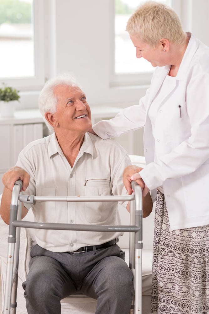 Professional carer helping her elderly patient to use a walking frame