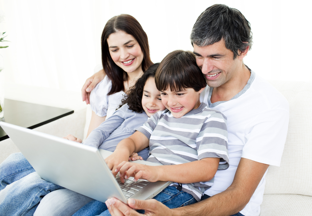 Glad family using a laptop sitting on sofa at home