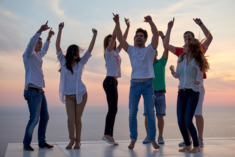 group of happy young people dancing and have fun on party in modern home bacony with sunset and ocean in background