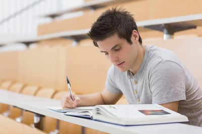 Student sitting reading a book and taking notes in lecture hall