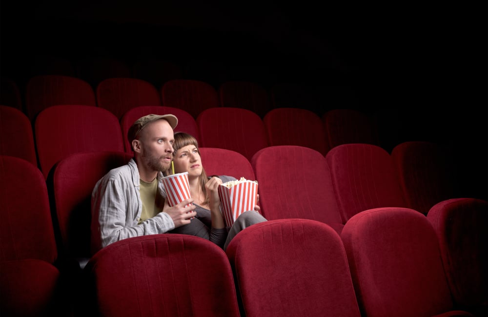 Young cute couple sitting alone at red movie theatre and having fun